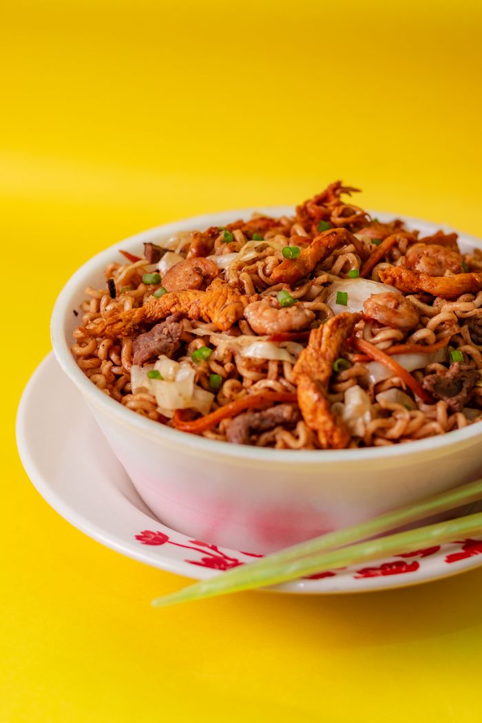 heros-img Appetizing chicken noodles in a colorful bowl on a yellow background, perfect for food blogs.