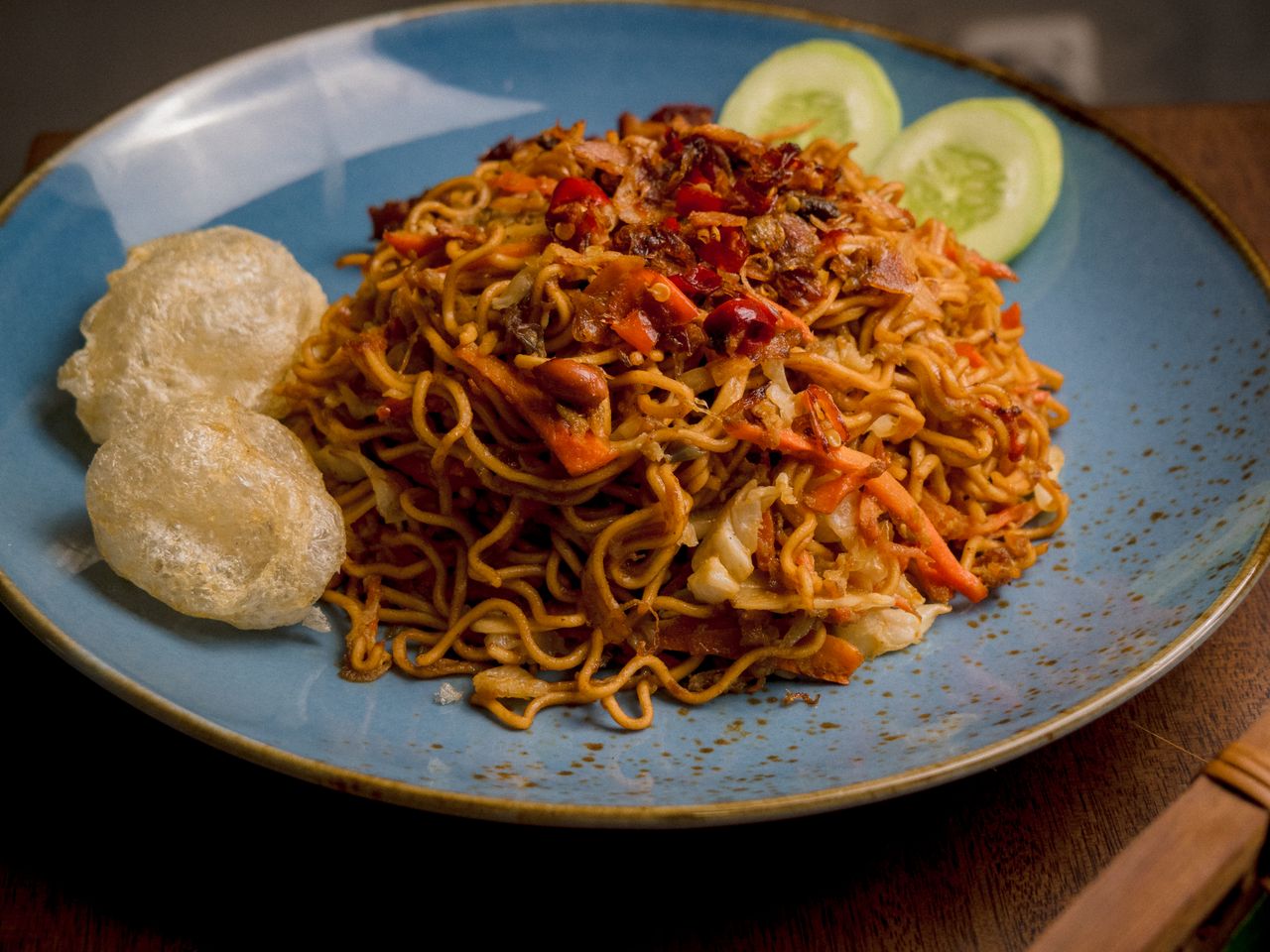 about-us-02 Delicious Indonesian Mi Goreng served with kerupuk on a plate.