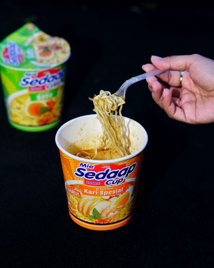 services-02 A hand lifts noodles from a flavorful curry spiced cup, ready to eat.