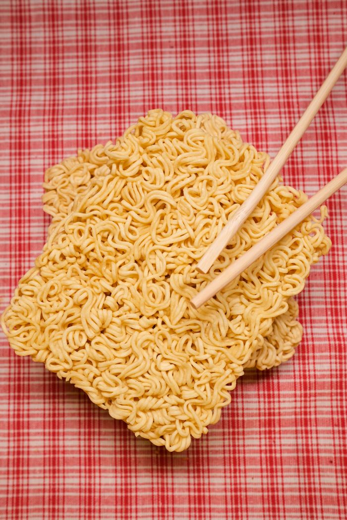 Top view of blocks of dried instant noodles and bamboo chopsticks placed on table covered with checkered napkin in kitchen
